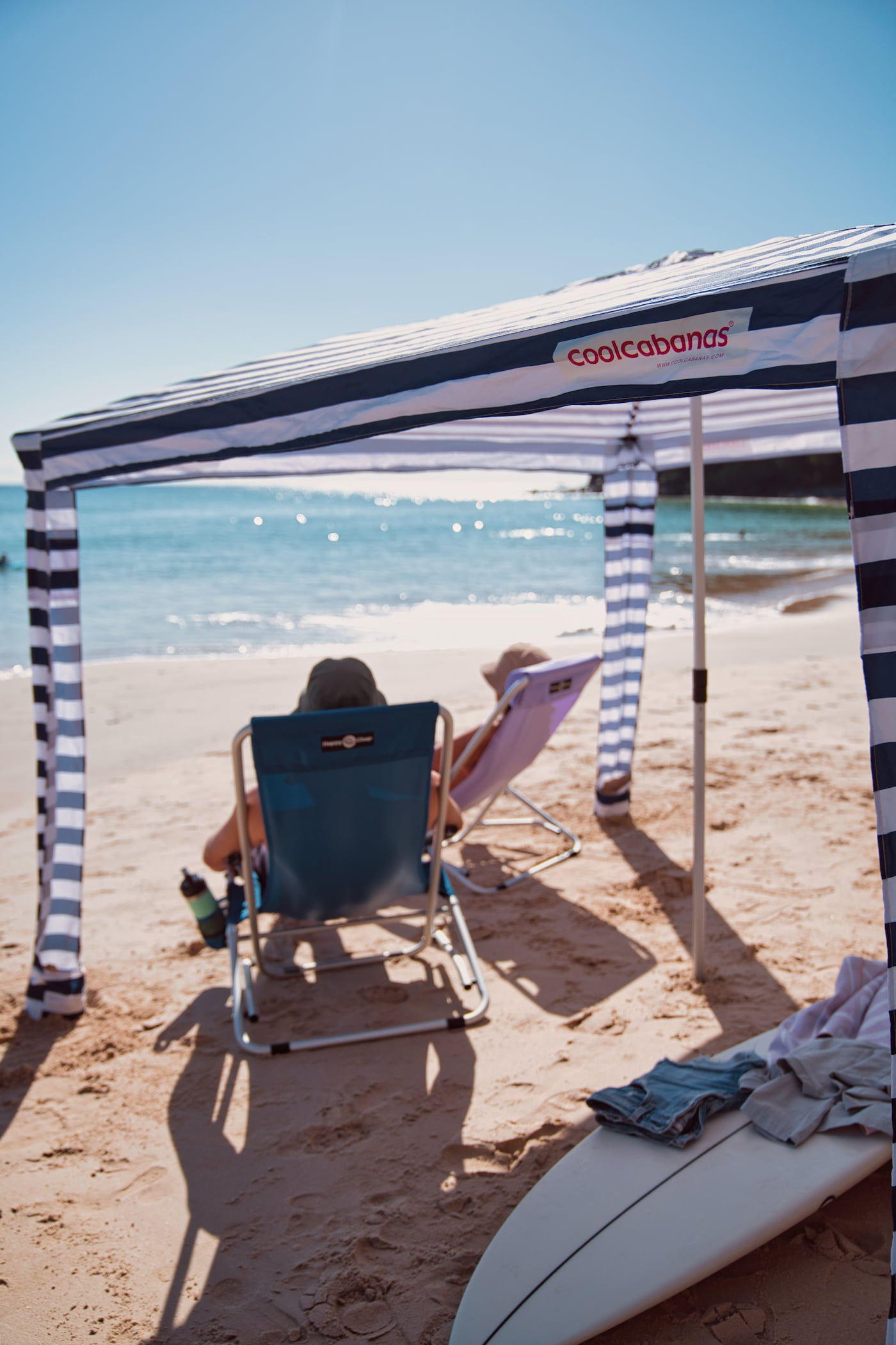 Two people sitting on bright beach chairs under a striped beach cabana